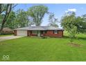Well-kept red brick home featuring a metal roof, attached garage, and lush green lawn at 679 Bark Dr, Anderson, IN 46011