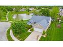 Aerial view of a home with a pond, lush green lawns, mature trees, and a two-car attached garage at 8121 Sand Ridge Cir, Indianapolis, IN 46237