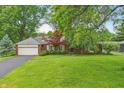 Charming brick home featuring an attached two-car garage, lush green lawn, mature trees, and professionally landscaped garden at 8752 Washington Blvd E Dr, Indianapolis, IN 46240