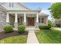 Inviting front porch featuring stone pillars and a red front door with lush landscaping at 15292 Slateford Rd, Noblesville, IN 46062