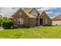 Brick two-story home featuring lush front lawn, decorative architectural details, and landscaped garden beds at 719 E New Rd, Greenfield, IN 46140