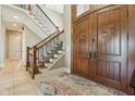 Grand foyer with a wooden staircase, detailed iron railings, tile flooring, and impressive wood double doors at 16332 Valhalla Dr, Noblesville, IN 46060