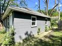 Grey cinder block detached garage with two windows and a white door in a green, tree filled yard at 4814 E New York St, Indianapolis, IN 46201