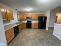 Kitchen boasts black appliances, oak cabinets, and neutral countertops, with vinyl flooring and a half wall to dining at 356 Seabreeze Cir, Avon, IN 46123