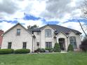 Beautifully landscaped white brick home with a lush green lawn, mature trees, and architectural details at 7823 Ashtree Dr, Indianapolis, IN 46259