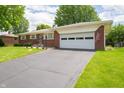 Classic brick home with attached garage and long driveway on a sunny day at 5903 Schoolwood Dr, Speedway, IN 46224