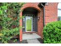 Close-up of arched brick entryway and green front door framed by lush greenery, inviting entrance to the home at 14492 Allison Dr, Carmel, IN 46033