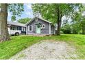View of cozy home with gray siding, green door, mature trees, and gravel driveway at 1841 New St, Indianapolis, IN 46203
