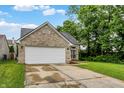 A well-maintained brick home with a two-car garage features a green lawn, mature trees, and a blue sky at 6010 Lakeside Manor Ave, Indianapolis, IN 46254