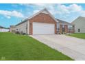 Side view of a brick home with a two car garage, manicured lawn and a paved drive at 107 Elliott Ave, Trafalgar, IN 46181