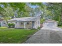 Inviting single-story home with a gravel driveway leading to a detached garage, surrounded by lush greenery and mature trees at 420 Vista Dr, Carmel, IN 46280