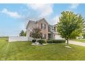 Inviting two-story home boasts a well-manicured lawn, lush trees, and a pristine white fence at 2260 Santa Fe Dr, Greenfield, IN 46140