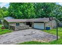 Aerial view of a stone ranch home featuring a two-car garage, mature trees, and a stone wall surrounding the front yard at 741 Fairway Dr, Indianapolis, IN 46260