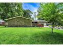 Side view of stone ranch home featuring a two-car garage, mature trees, and a stone wall surrounding the front yard at 741 Fairway Dr, Indianapolis, IN 46260