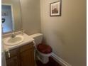 Compact powder room featuring a single sink vanity, toilet with dark maroon cover, and neutral decor at 11621 Coastal Dr, Indianapolis, IN 46229