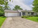 Ranch-style home with attached garage and a large driveway surrounded by lush landscaping and mature trees at 3004 N Timber Ln, Muncie, IN 47304