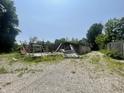 View of a partially collapsed building surrounded by gravel, vegetation, and trees on a clear day at 4566 Melbourne Rd, Indianapolis, IN 46228