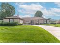 Beautiful brick ranch home with mature trees, curved driveway, manicured lawn and American flag at 8209 Burn Ct, Indianapolis, IN 46217