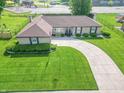 Aerial view of brick ranch home on manicured lot with curved driveway, mature trees, and front garden at 8209 Burn Ct, Indianapolis, IN 46217
