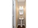 Cozy half-bath features a pedestal sink, round mirror, decorative lighting, and wood-look flooring at 5767 Bluff View Ln, Whitestown, IN 46075