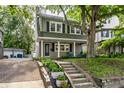 Inviting home with a covered front porch, surrounded by lush greenery and mature trees on a sunny day at 4619 N Park Ave, Indianapolis, IN 46205
