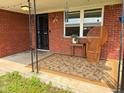 Inviting covered porch with brick surround, adorned with a stylish wicker chair and floral rug at 8990 N 850 W, Fairland, IN 46126