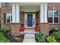 Inviting front porch showcasing brick pillars, a vibrant blue door, and charming flower-filled planters at 5441 Ellsworth Dr, Plainfield, IN 46168
