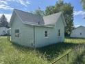 Rear view of a green house featuring siding, windows with white shutters, and overgrown lawn at 1739 E 18Th St, Anderson, IN 46016