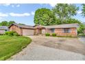 Single story brick home featuring an attached garage, concrete driveway, and lush green landscaping at 407 Woodland E Dr, Greenfield, IN 46140