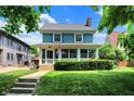 Beautiful home featuring a lush green lawn, vibrant landscaping, and a cozy enclosed front porch, located on a tree lined street at 140 W Hampton Dr, Indianapolis, IN 46208