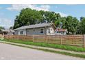 Street view of a home featuring a natural wood fence, grassy lawn, and mature trees against a blue sky at 802 N Tuxedo St, Indianapolis, IN 46201