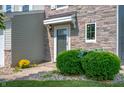 A stone accented entry featuring an olive-colored front door framed by manicured bushes and yellow flowers at 3010 Underwood Ct, Whiteland, IN 46184