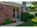 A welcoming front porch with an American flag, brick facade, and blooming flowers at 1510 Dominion Dr, Zionsville, IN 46077