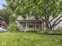 View of a two-story home with charming front porch, American flag, and mature tree shading the lawn at 4455 Central Ave, Indianapolis, IN 46205