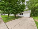 Quaint one-story house featuring an attached garage and a long driveway, surrounded by lush greenery at 308 Mohawk St, Anderson, IN 46012