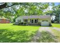 Traditional single-story home featuring an attached garage, stone accents, and a lush green yard with mature trees at 7600 S Oak Dr, Indianapolis, IN 46227