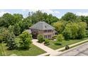 Aerial view of a brick house with well-manicured lawn, driveway and mature trees at 4529 Panthera Leo Dr, Carmel, IN 46074
