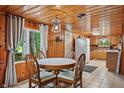 Dining area with wooden walls, a round table set, a window view, and kitchen access at 4418 North Dr, Quincy, IN 47456
