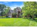 Landscaped front yard with mature trees surrounding a brick home with a three-car garage and well-manicured lawn at 7648 W Williamswood Dr, New Palestine, IN 46163