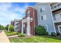 Attractive condo complex featuring brick accents, white pillars, green grass, and blue siding under a partly cloudy, sunny sky at 5011 Amber Creek Pl # 310, Indianapolis, IN 46237