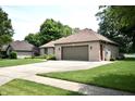 Brick home featuring a two-car garage, surrounded by a green lawn and mature trees, offering a serene setting at 5943 Red Maple Dr, Indianapolis, IN 46237
