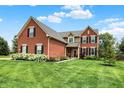 Charming red brick home featuring green grass, black shutters, and colorful flowers on the front porch at 13191 Roma, Carmel, IN 46074
