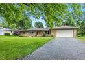 Single-story home featuring an attached garage, well-maintained lawn, mature landscaping, and a cracked asphalt driveway at 5205 Staughton Dr, Indianapolis, IN 46226