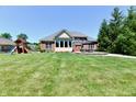 Expansive backyard featuring a patio, play structure, lush lawn, and mature trees at 7413 Misty Woods Ln, Indianapolis, IN 46237