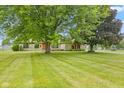 Lush front yard featuring large trees that frame the stone home with a decorative wood door at 5550 W Mooresville Rd Byp, Indianapolis, IN 46221