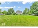 Home featuring a large front lawn, mature trees, and a gravel driveway under a sunny, partly cloudy sky at 1130 E 105Th St, Carmel, IN 46280