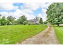 Home with a large front lawn, mature trees, and a gravel driveway set against a blue sky at 1130 E 105Th St, Carmel, IN 46280