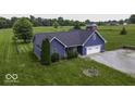An aerial view shows a blue home with a spacious lawn, driveway, and mature trees at 911 Centennial Rd, Martinsville, IN 46151