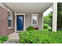 Inviting covered porch with a vibrant blue front door, complemented by lush greenery and brick accents at 9477 Aberdare N Dr, Indianapolis, IN 46250