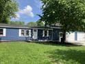 Blue home featuring white trim, lush lawn, and mature trees, with a convenient two-car garage at 221 N 9Th St, Elwood, IN 46036